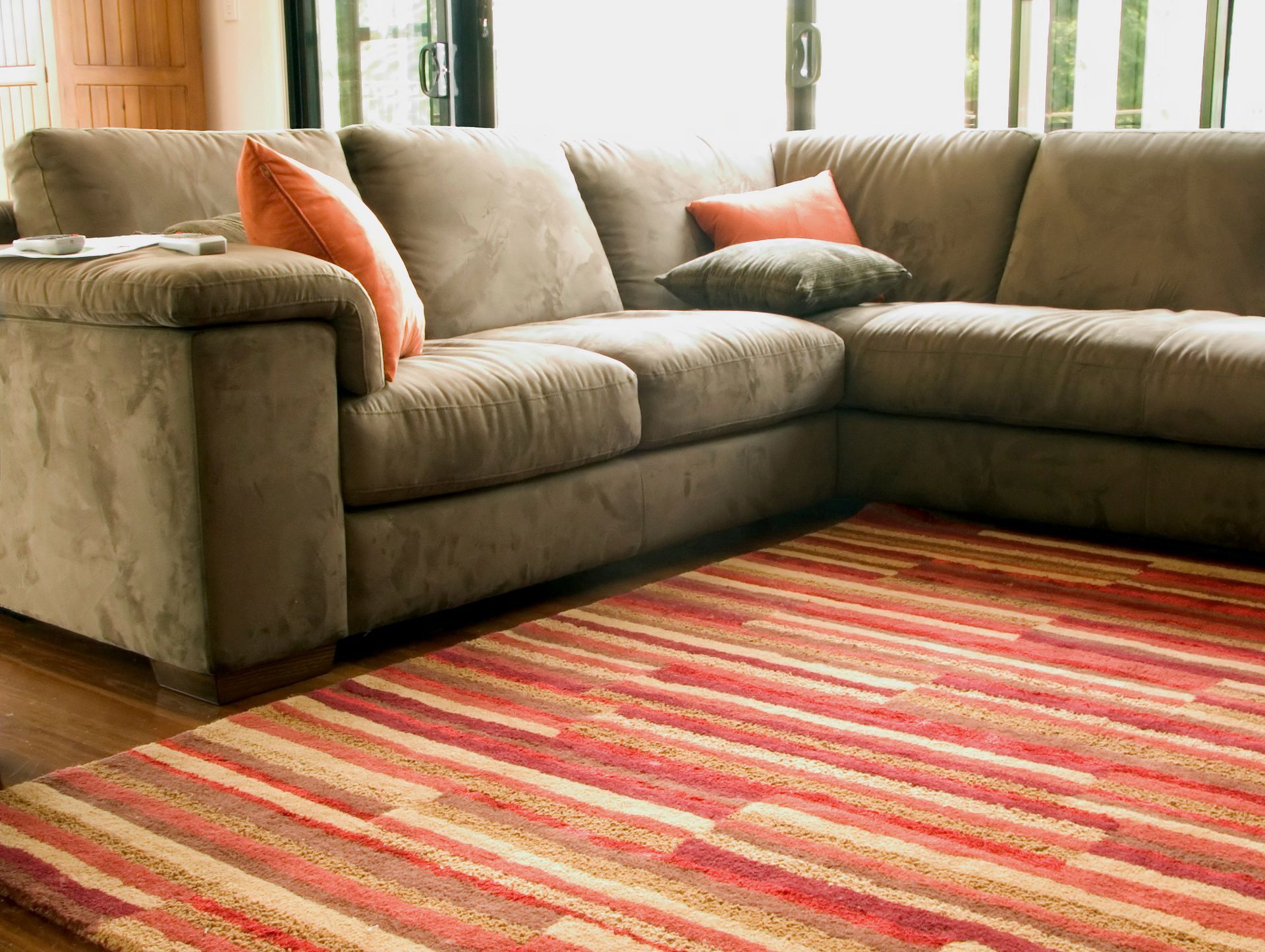 Brown sectional sofa with orange and gray pillows on a red and beige striped rug.