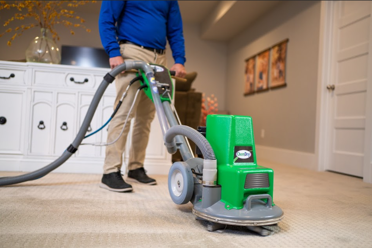Man operating a green carpet cleaning machine in a room with beige carpet.