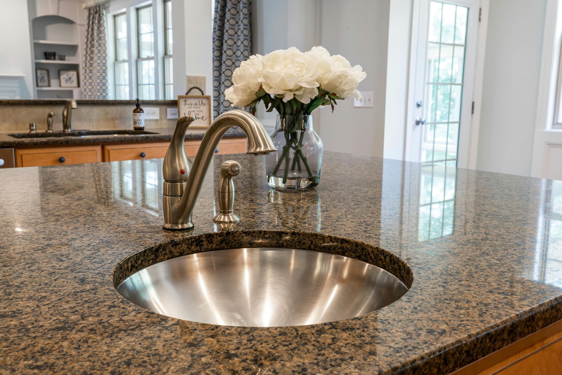 Kitchen island with a stainless steel sink, faucet, granite countertop, and flowers.