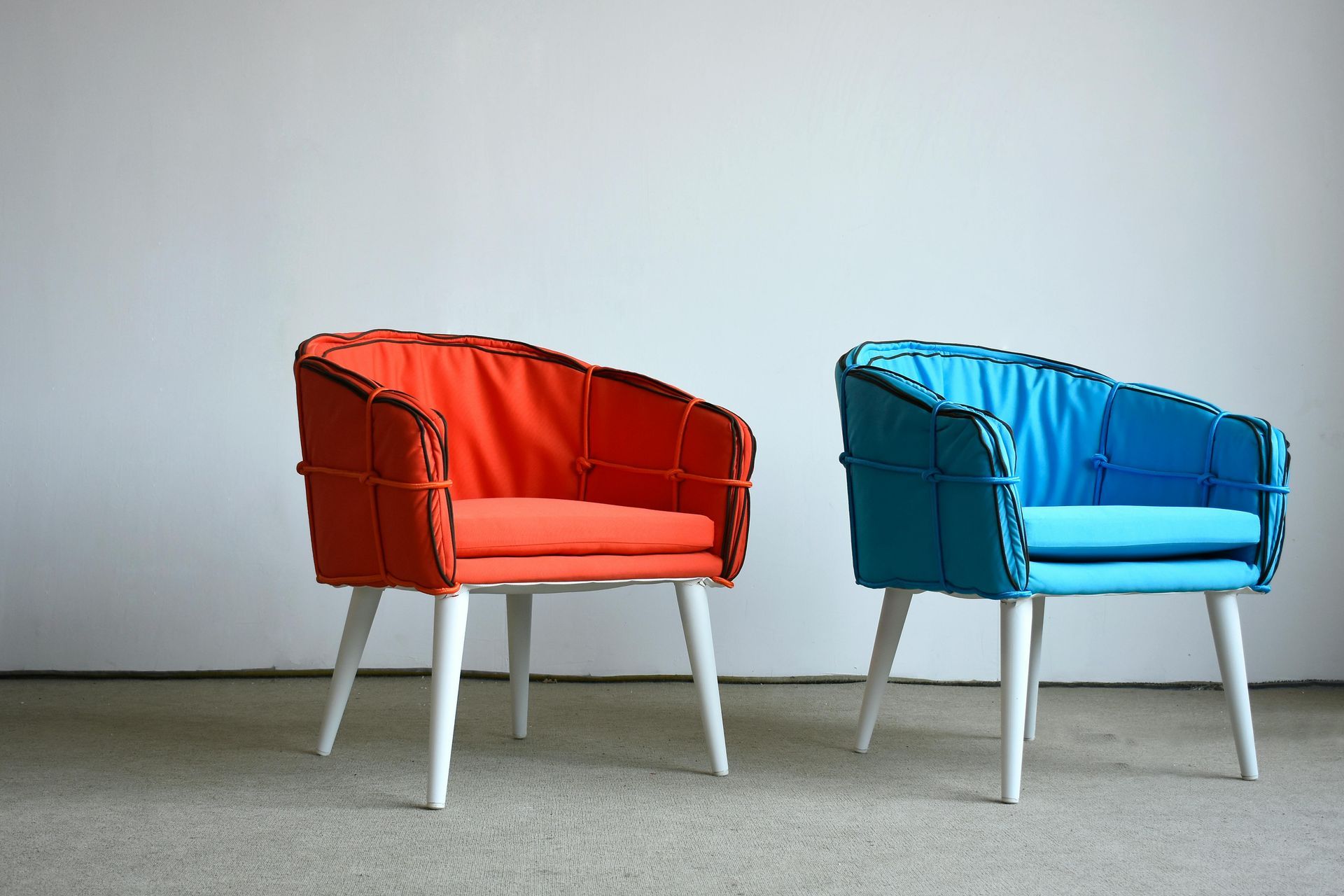 Two modern armchairs, one orange and one blue, with white legs, against a white wall.