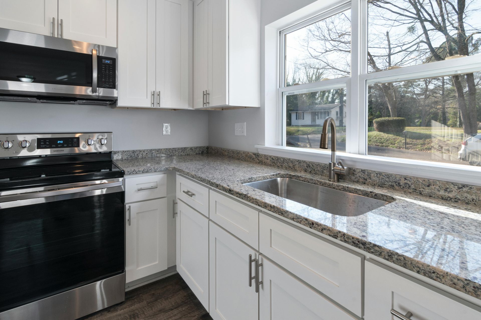 White kitchen with stainless steel appliances, granite countertops, and a window overlooking trees.