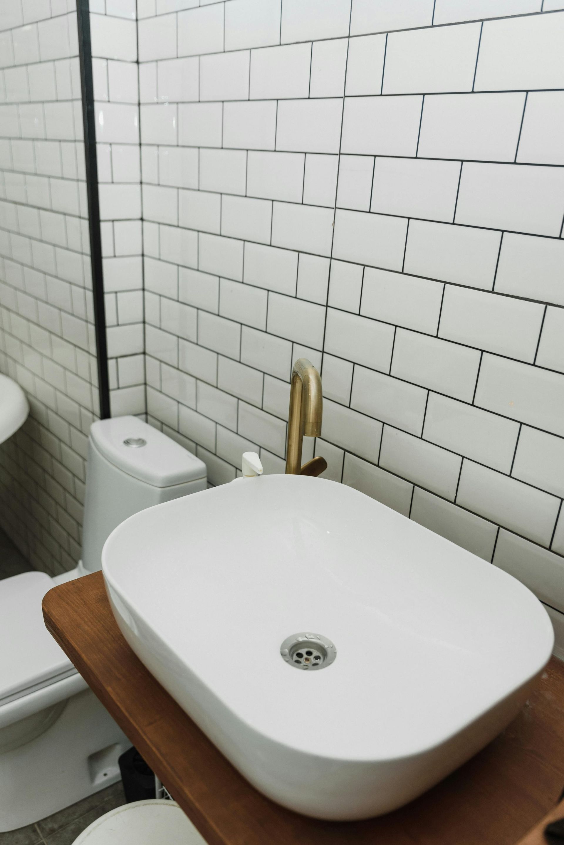 White oval sink with gold faucet on wooden counter, white subway tile wall.