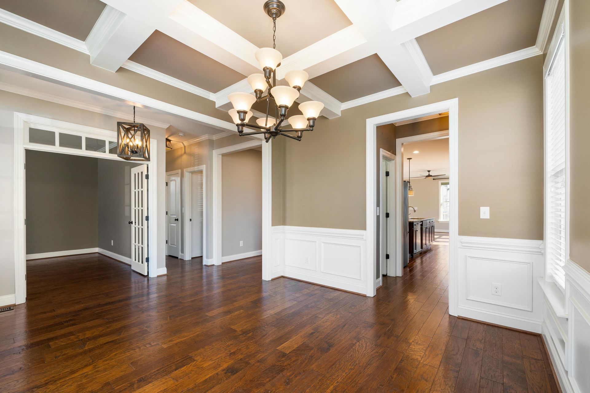 Empty dining room with dark wood floors, white trim, and a coffered ceiling.