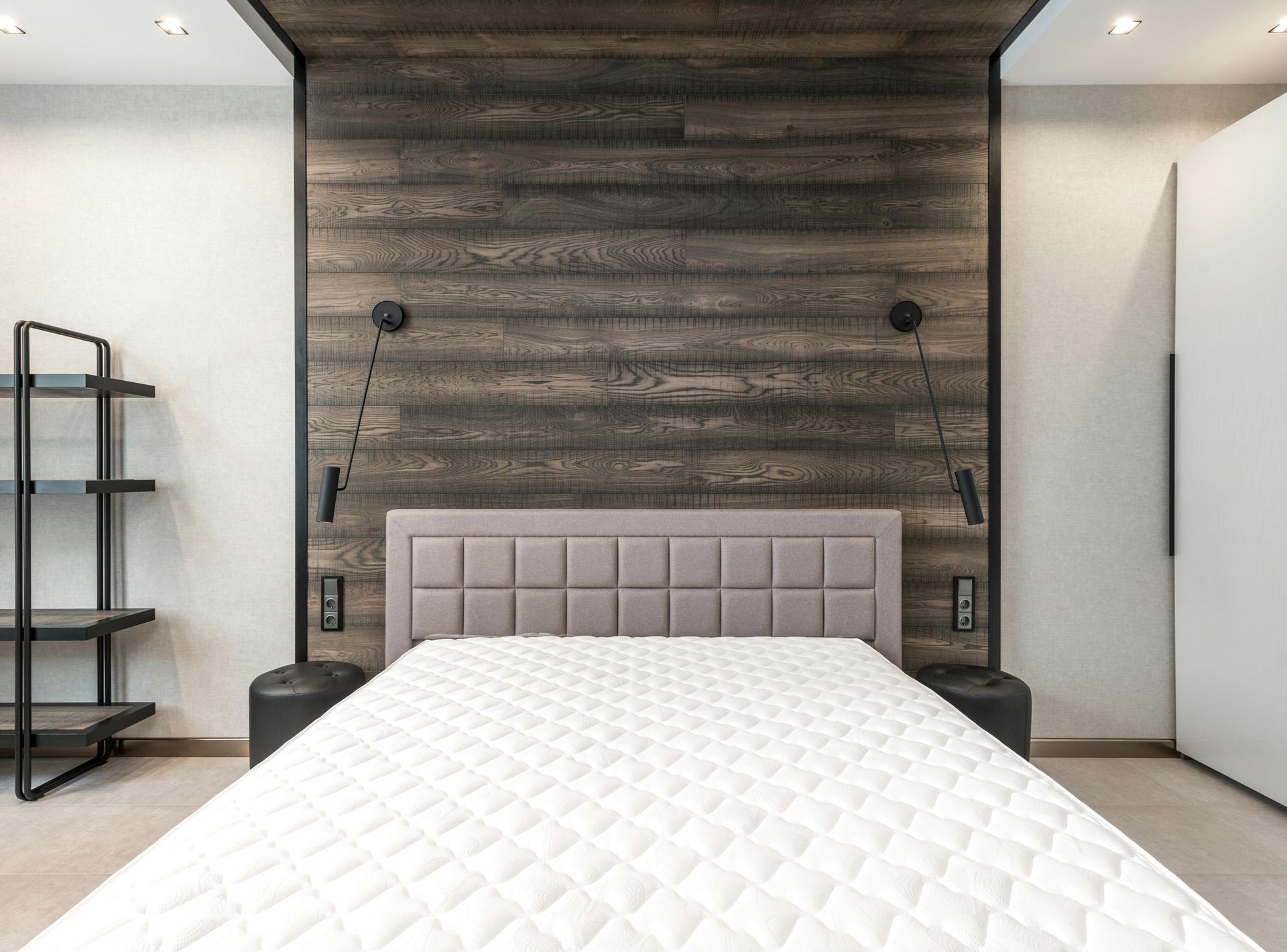 Bedroom with wood accent wall, bed, lamps, and black shelving.