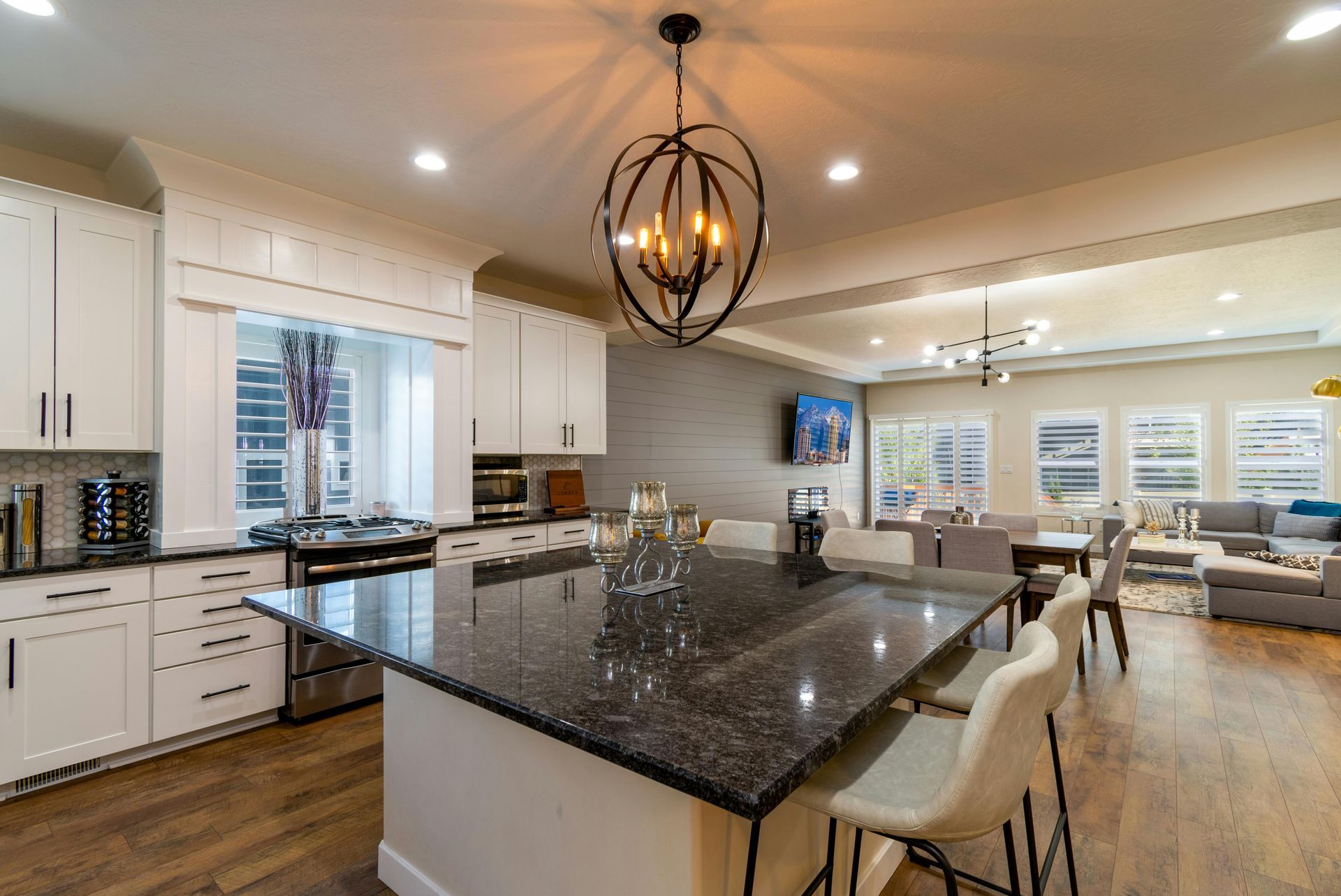 Modern kitchen with island, white cabinets, granite countertop, and chandelier, opening to a living area.