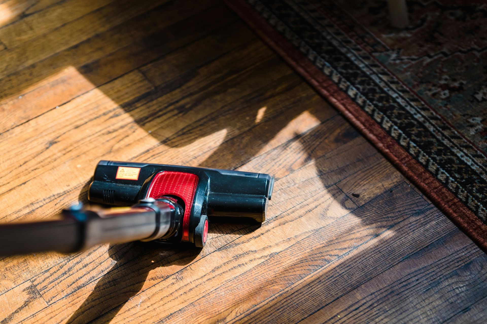 Vacuum cleaner cleaning hardwood floor next to a patterned rug.