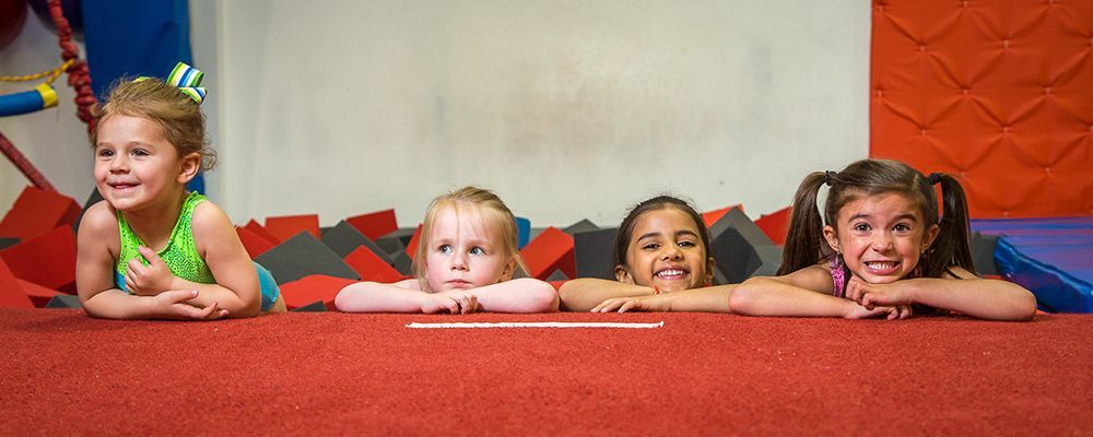 Four children smiling, resting arms on red surface, looking at something off camera.