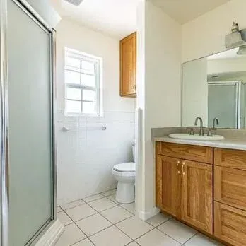 Small bathroom with shower, toilet, window, and wood vanity with mirror.