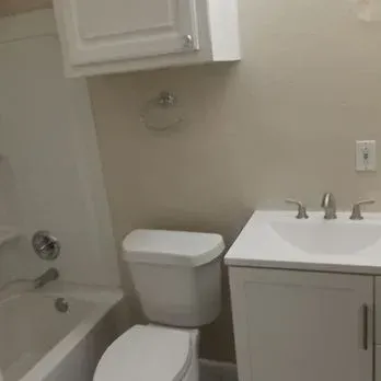 Small beige bathroom with toilet, sink, bathtub, and white wall cabinet.