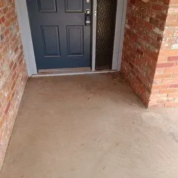 Front porch with a dark blue door, brick walls, and a concrete entryway.