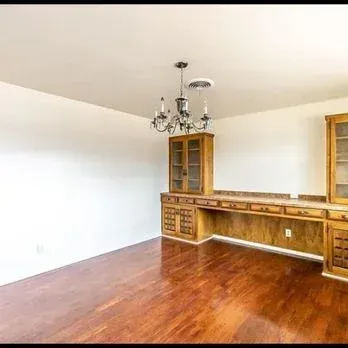 Empty dining room with hardwood floors, white walls, wood built-in bar, and chandelier.