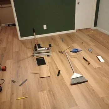 Scattered tools and floorboards on a wood floor, with a green wall and door in the background.
