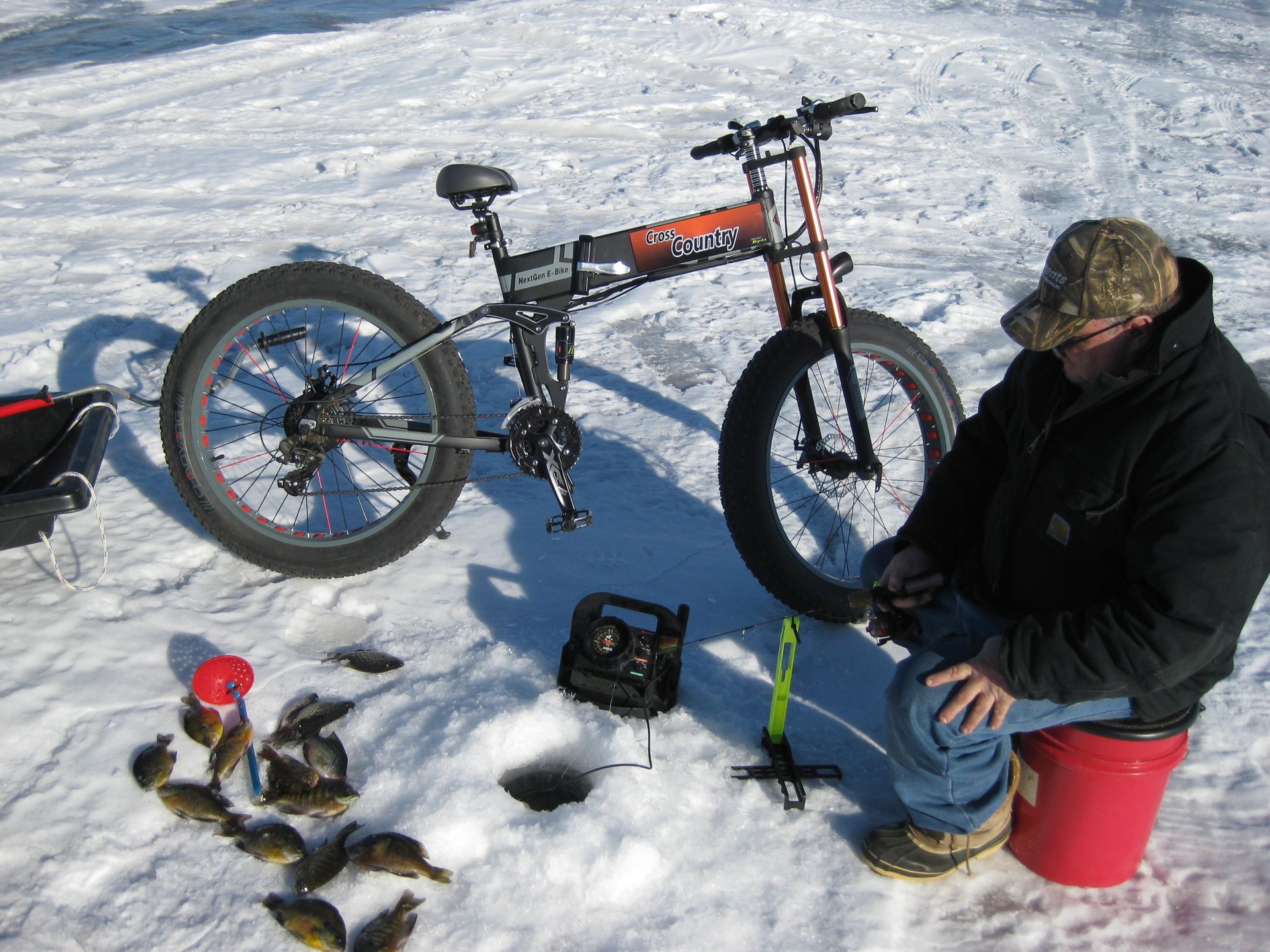 A man is fishing in the snow next to a bicycle