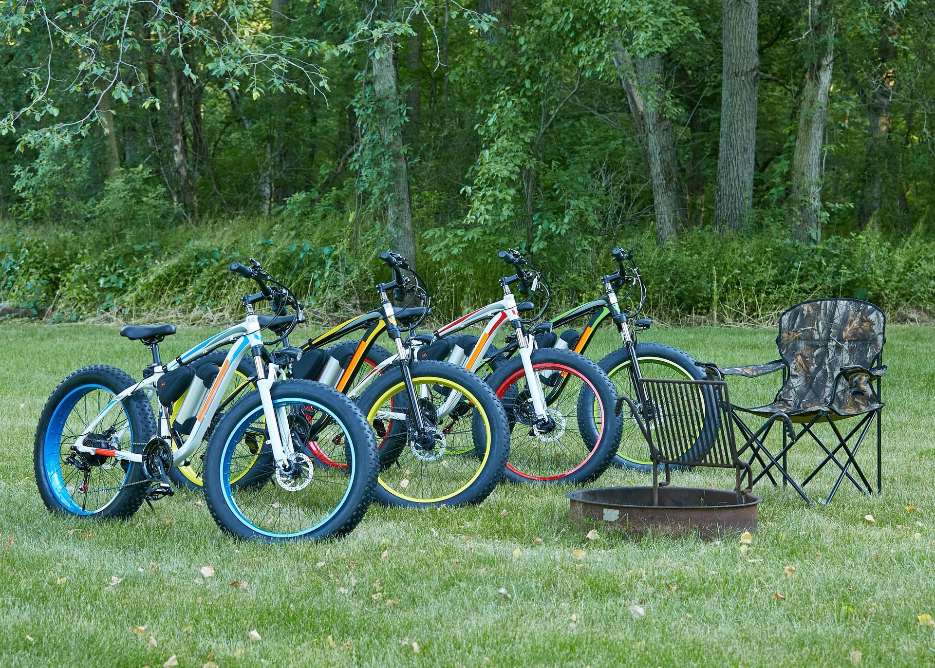 A row of bicycles are parked in a grassy field next to a fire pit.