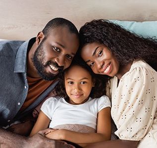 A man , woman and child are laying on a bed and smiling for the camera.