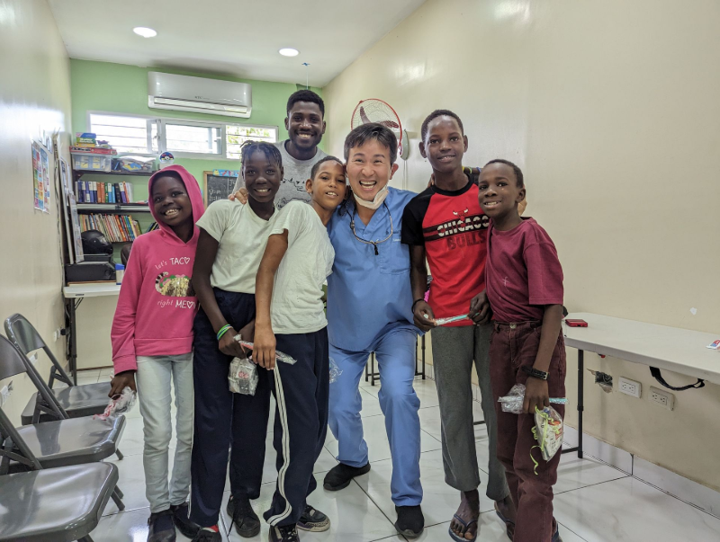 Six people smiling in a clinic hallway, standing together near exam tables and bookshelves.