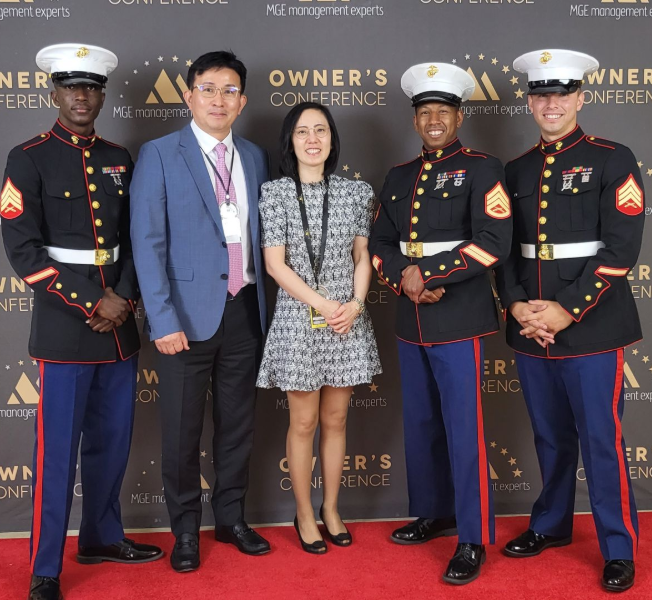 Five people posing on a red carpet in front of a branded backdrop, including four uniformed officers and one woman in a dress