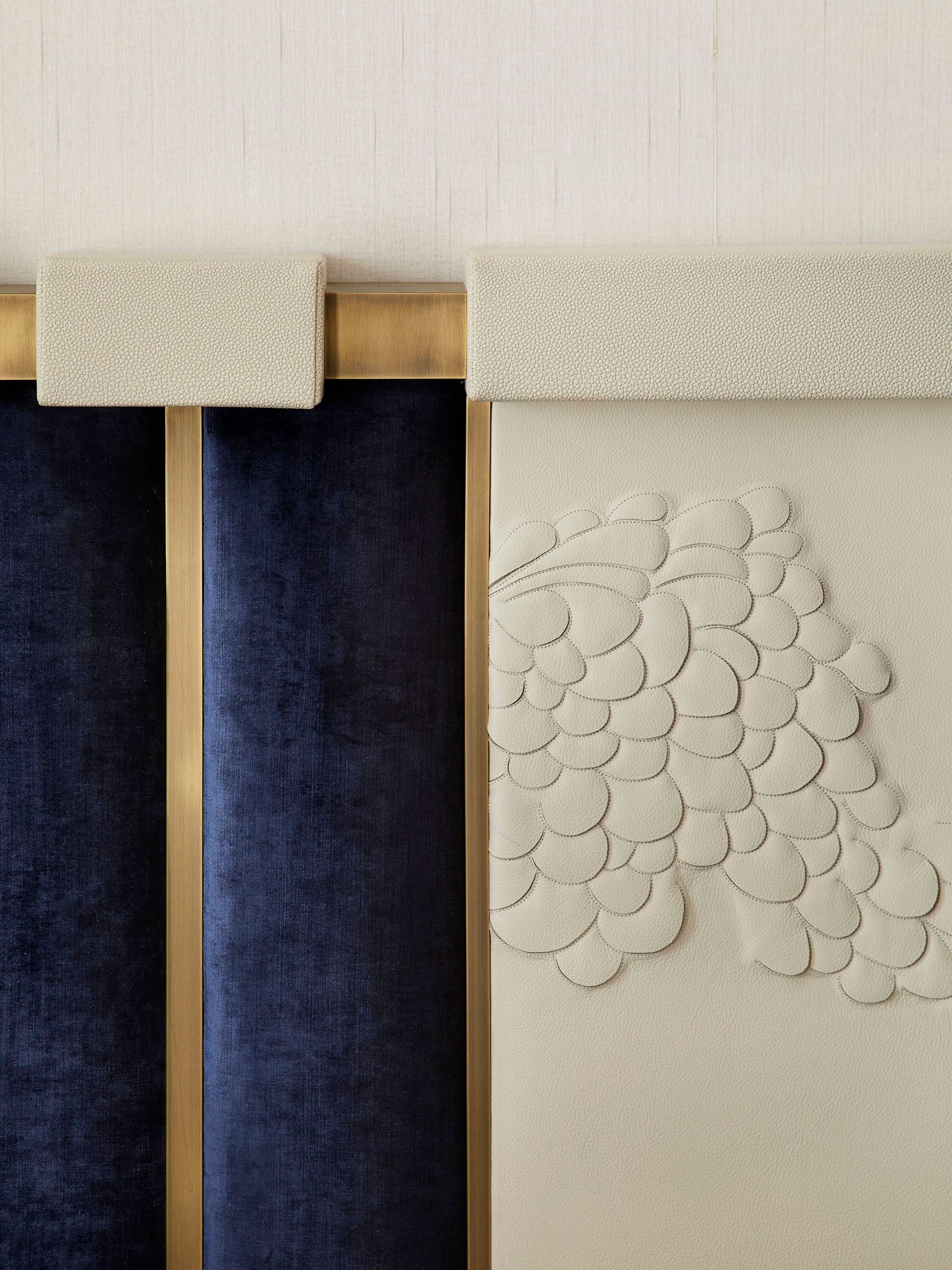 Close-up of textured headboard with blue velvet panels and embellished cream section, accented by gold trim.