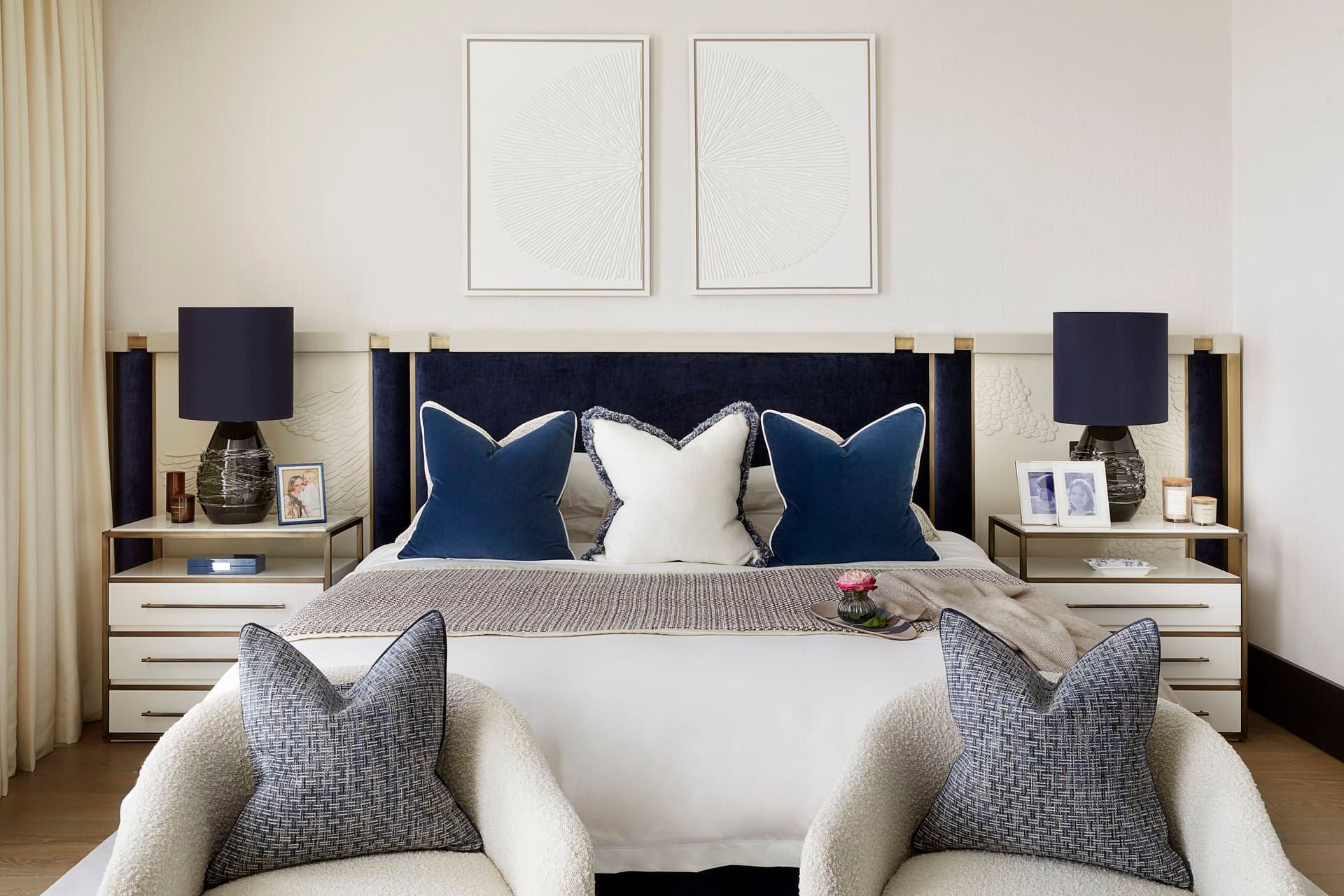 Luxurious bedroom with navy headboard, matching lamps, white and blue pillows, and two armchairs.