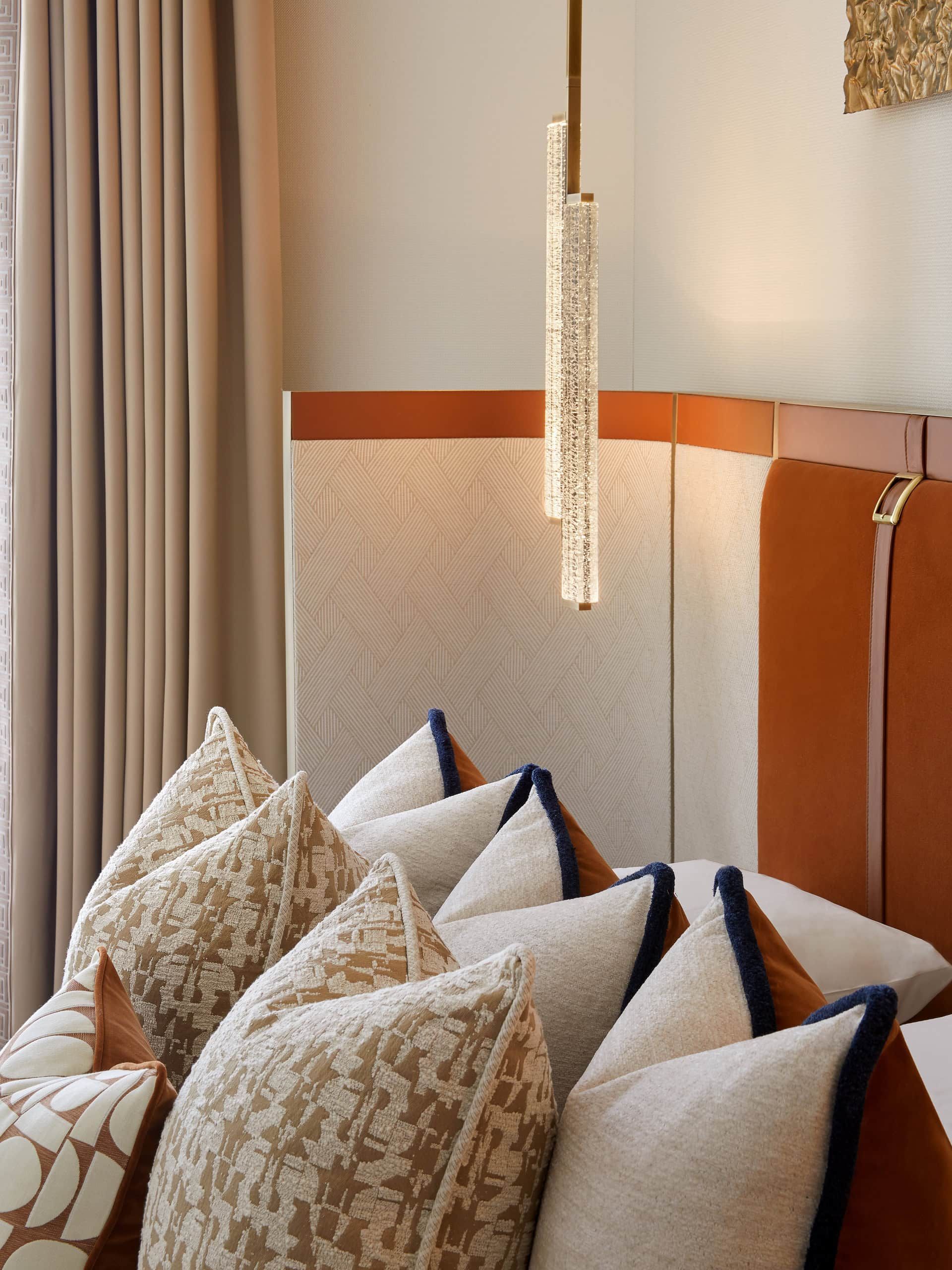 Bedroom with pillows, pendant light, and orange headboard.