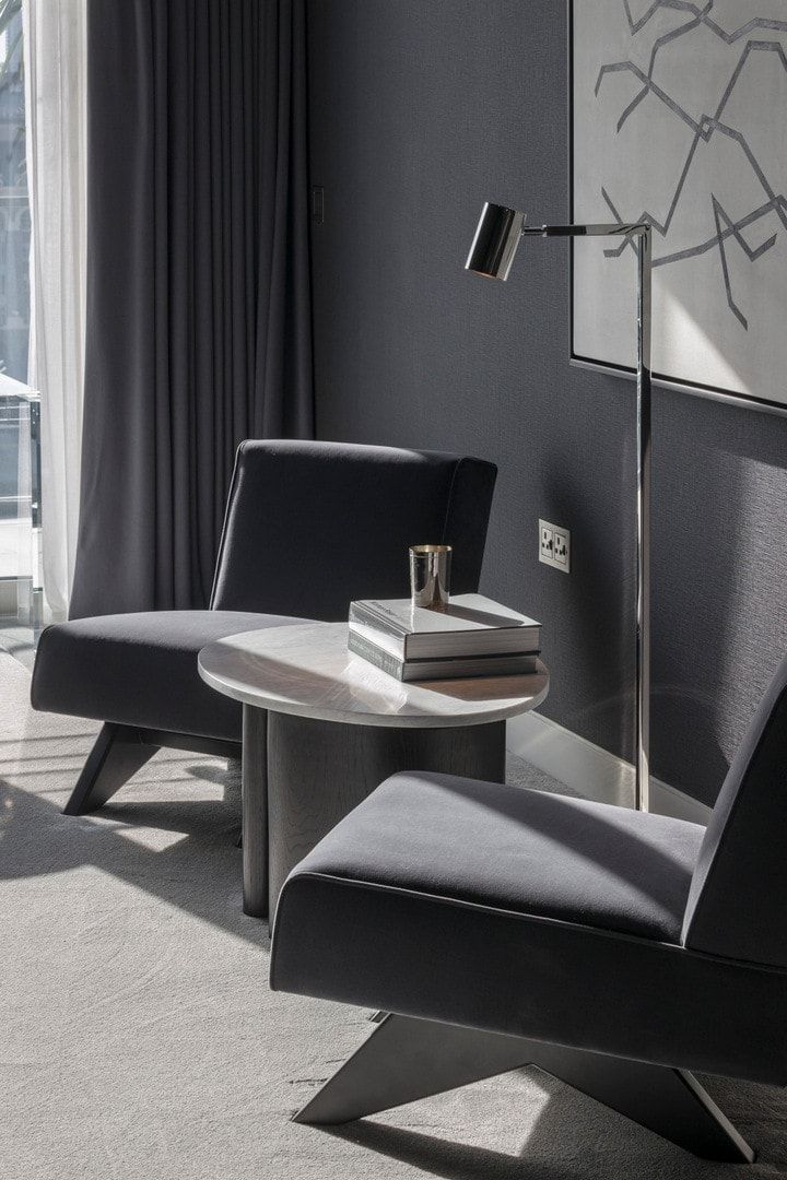 Two gray armchairs flanking a marble side table in a room with a lamp, art, and a window.