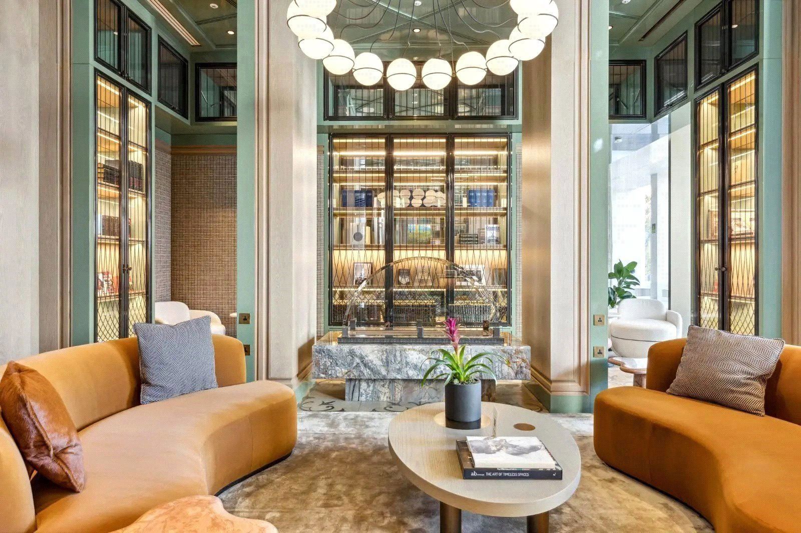 Elegant lounge with orange sofas, marble bar, and circular chandelier.