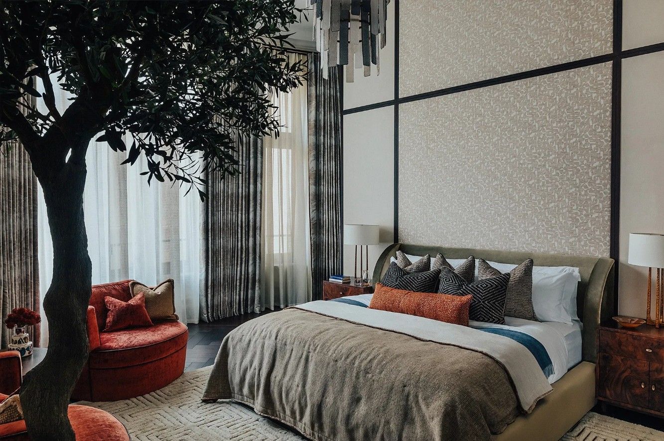 Luxurious bedroom with a tree, bed, red chair, and patterned wallpaper.