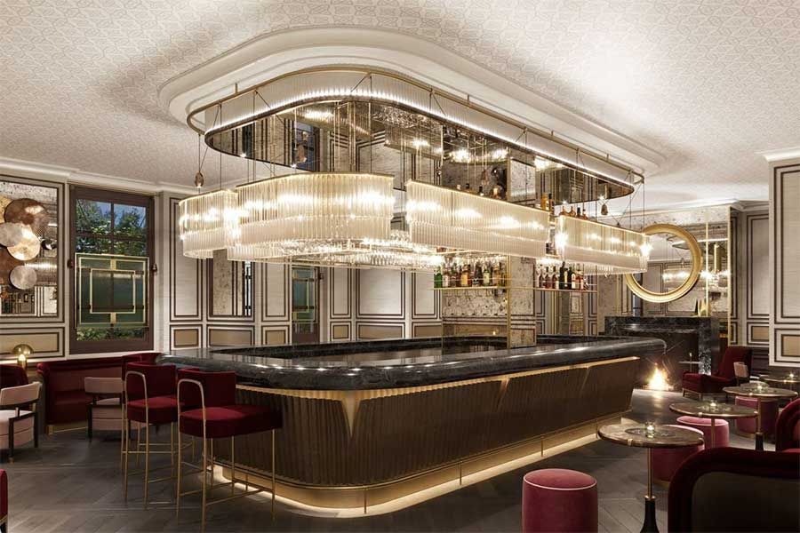Elegant bar interior with chandeliers, dark bar, red velvet stools, and small tables.