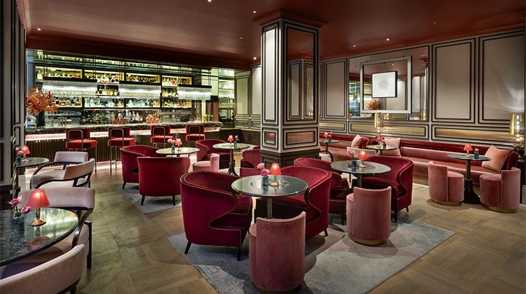 Elegant bar with red velvet seating, a well-lit bar, and marble-topped tables, in a dark red and gold interior.