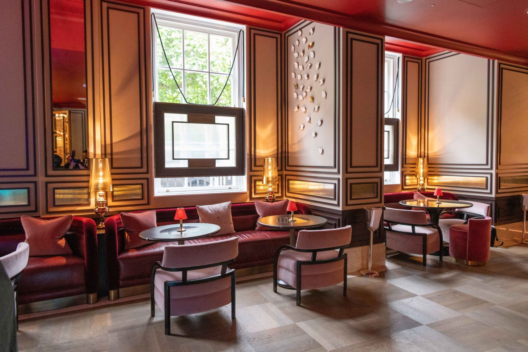 Elegant lounge with velvet seating, round tables, and framed windows. Red and gold accents throughout.