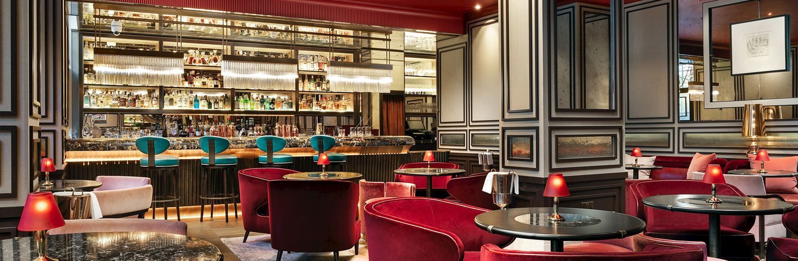 Luxurious red bar with velvet chairs, turquoise bar stools, and a well-stocked bar in a dimly lit room.