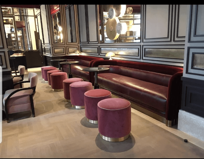 A bar with burgundy seating, including a long sofa and round stools, against a gray panelled wall.