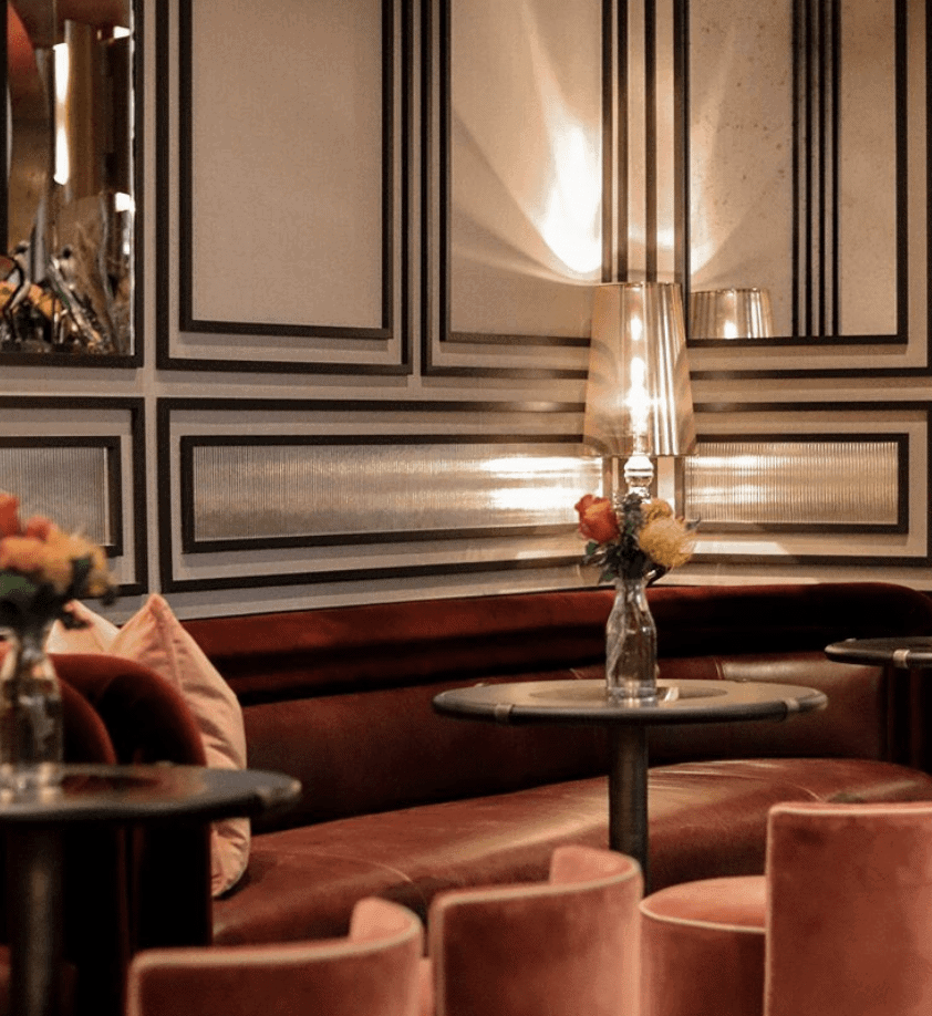 Cozy bar seating with red velvet booths, small tables, and floral arrangements. Decorative wall panels and ambient lighting.
