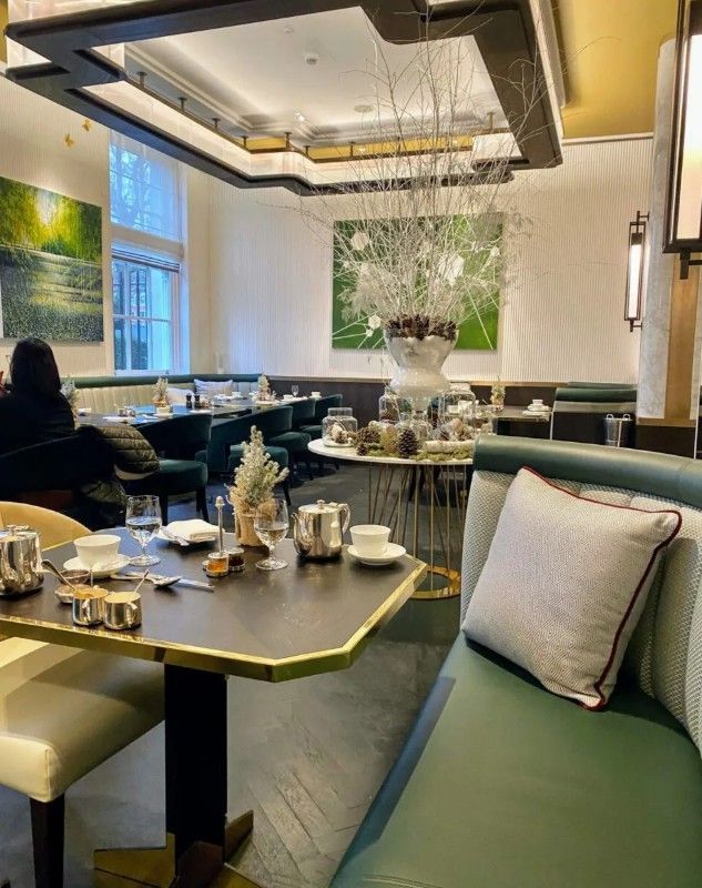 Elegant dining room with green banquette seating, tables set for tea, and modern art.