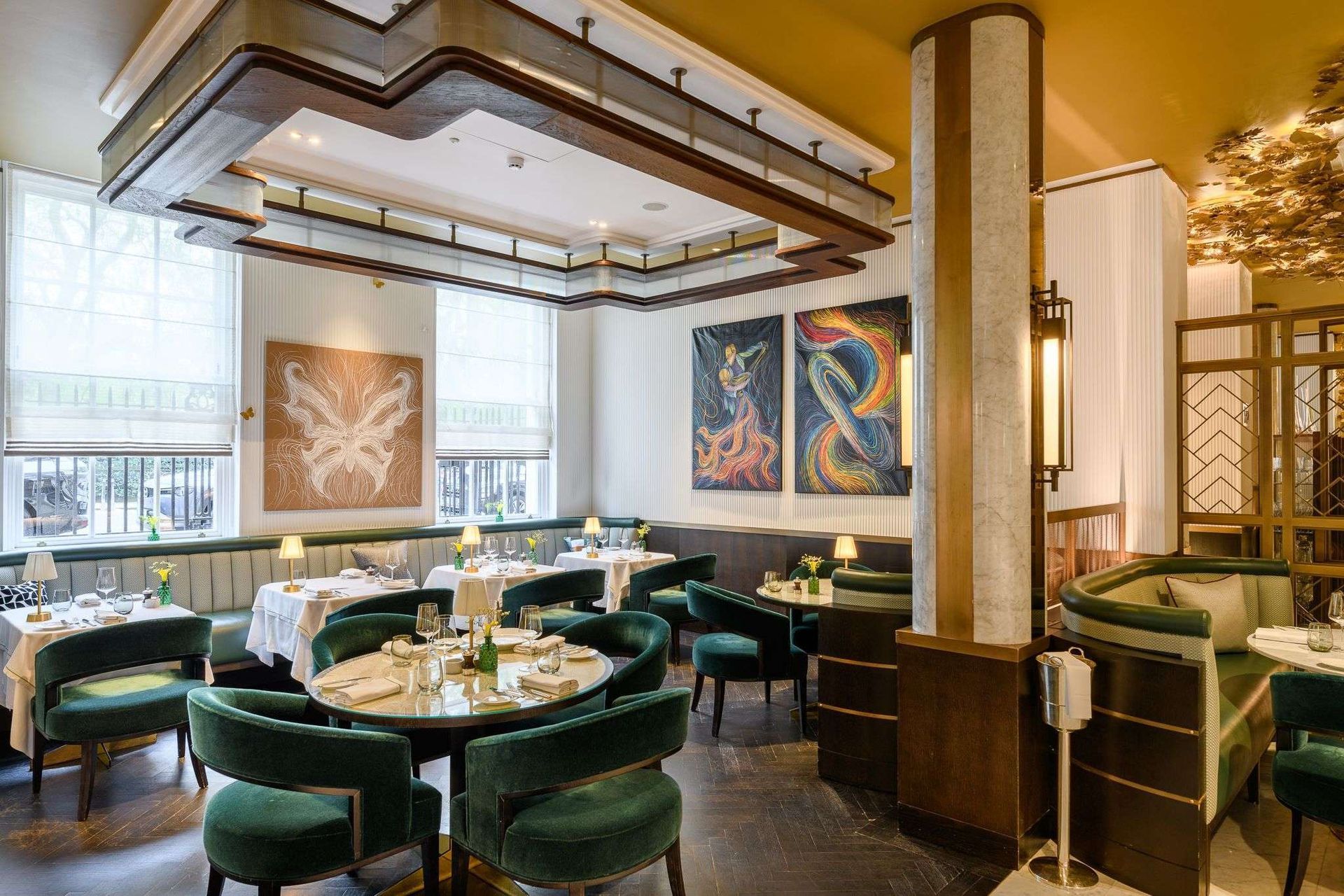 Elegant restaurant interior with green velvet chairs, round tables, artwork, and warm lighting.