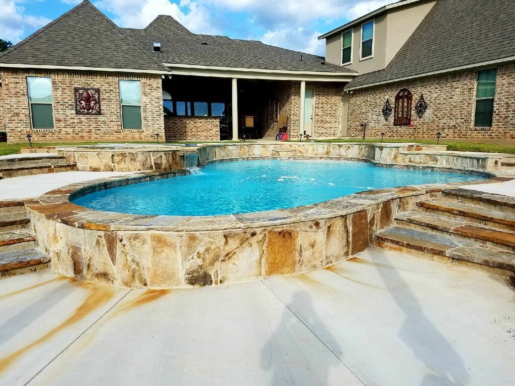 A large swimming pool is in front of a large brick house.