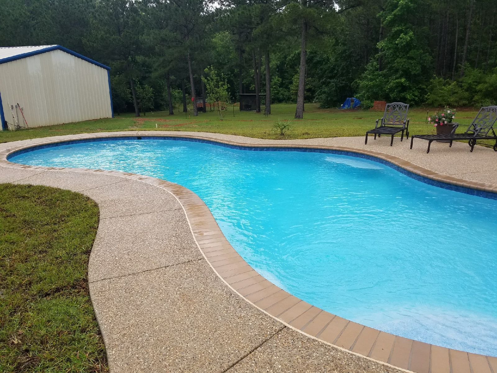 A large swimming pool is surrounded by lawn chairs and a building.