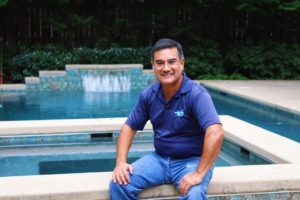 A man is sitting on a ledge next to a pool.