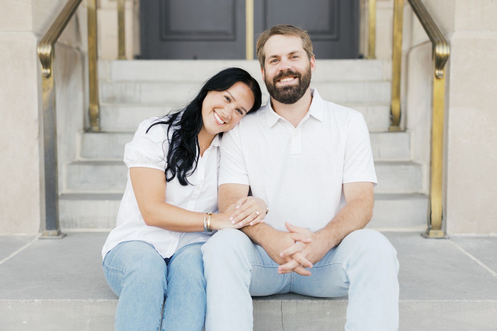 Couple sitting on steps, woman leaning on man's shoulder, smiling. They are holding hands.