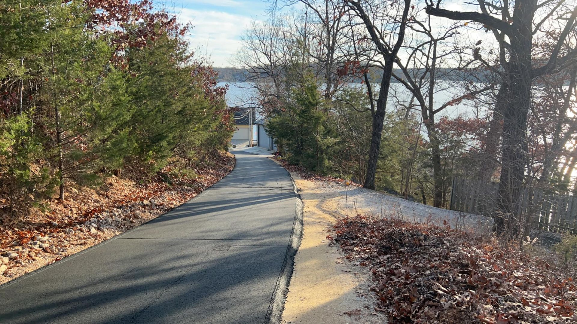A road going through a forest next to a body of water.