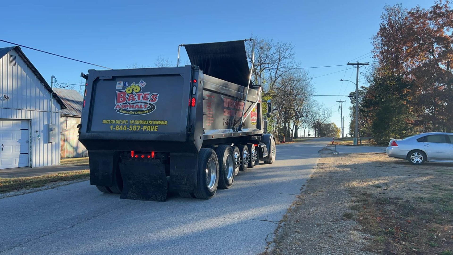 A dump truck is driving down a road next to a white car.
