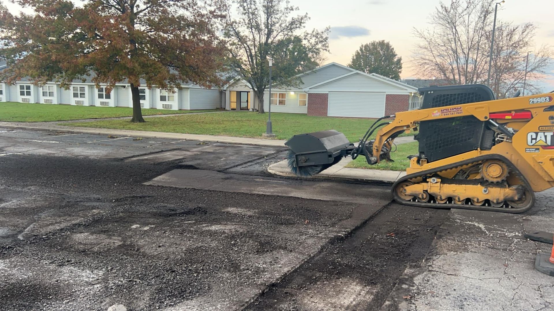 A yellow cat bulldozer is laying asphalt in a parking lot.
