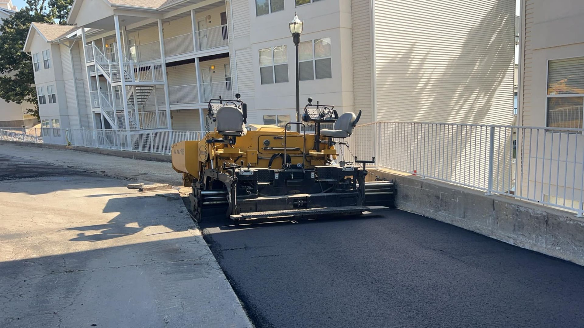 A machine is laying asphalt on a street in front of a building.
