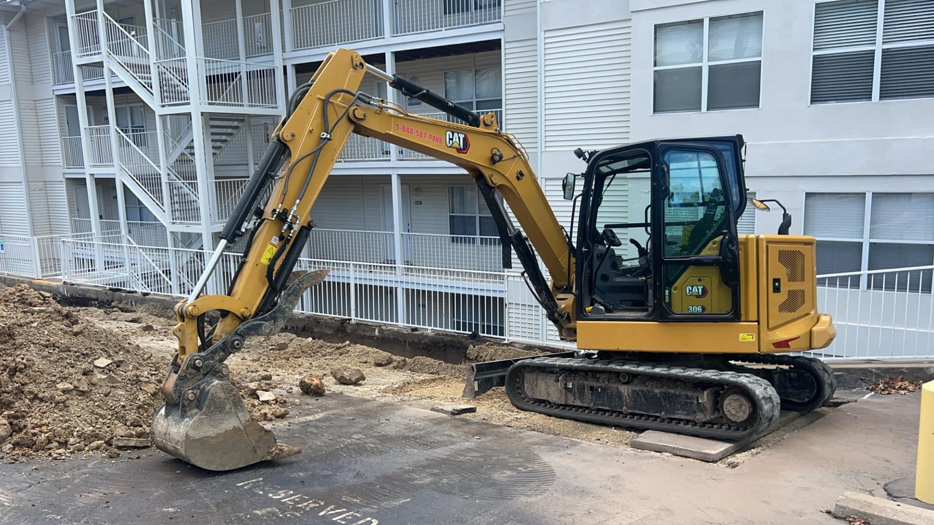 A yellow excavator is sitting in front of a building.