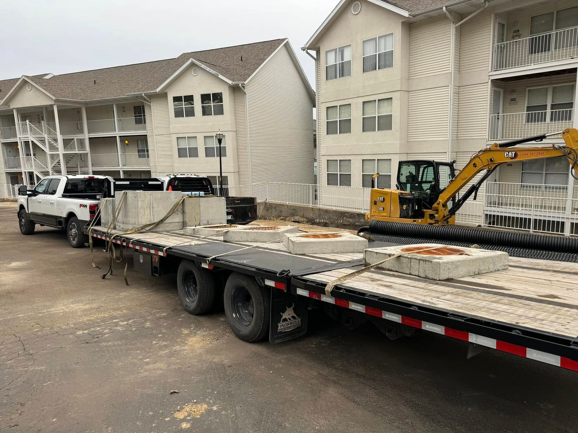 A truck is carrying a trailer with concrete blocks on it in front of a building.