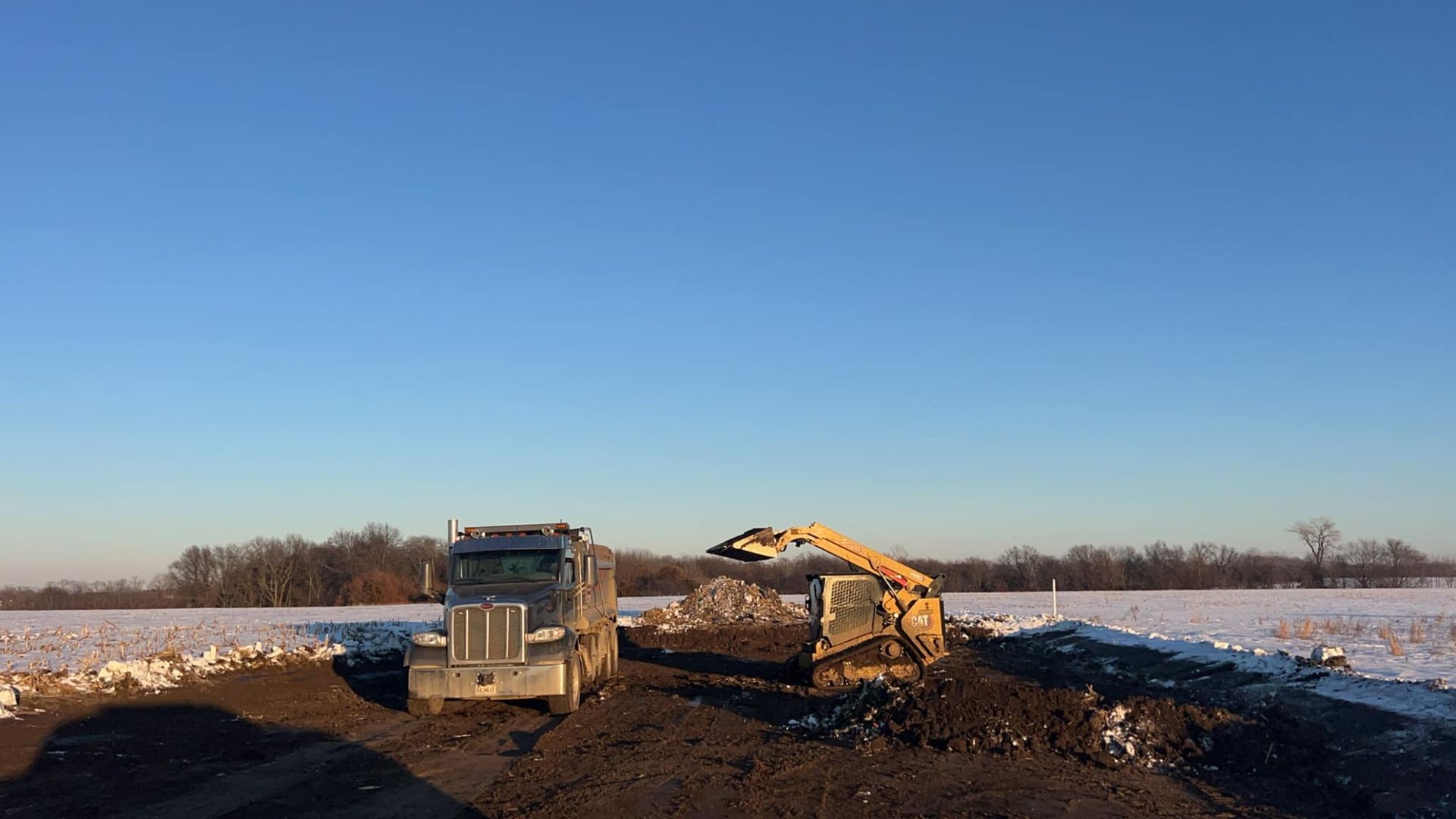 A dump truck and an excavator are sitting in a dirt field.