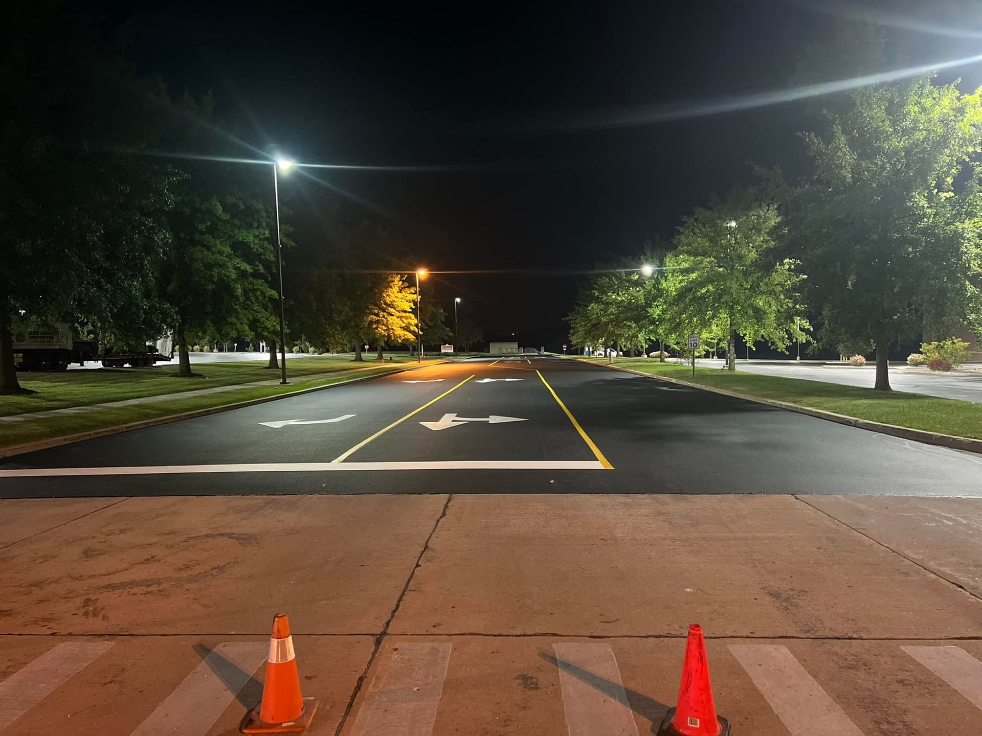 Two orange traffic cones are on the side of a road at night