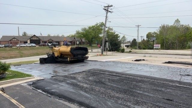 A yellow truck is laying asphalt on the side of a road.