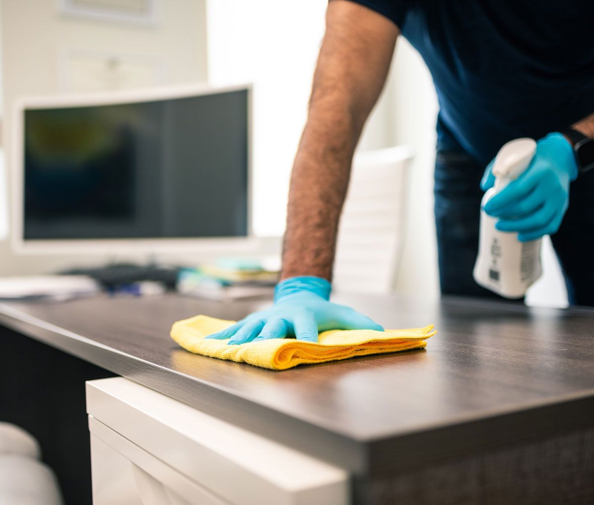 A man wearing blue gloves is cleaning a desk with a cloth