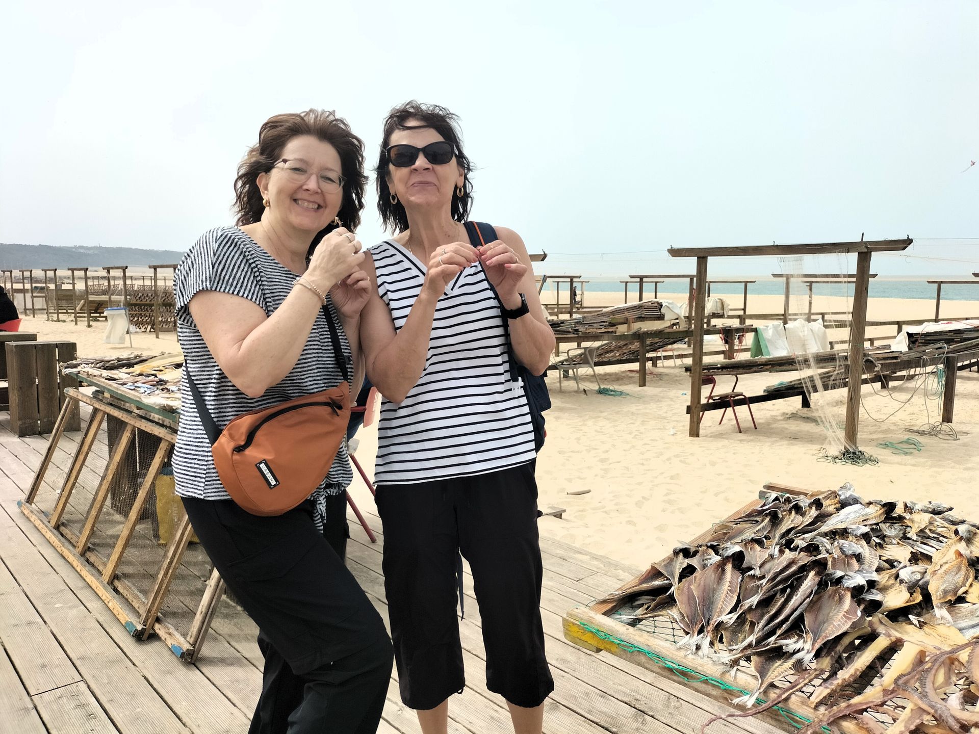 A group of happy travelers on the beach of Nazarรฉ in Portugal, next to the typical natural fish drying point during a tour.